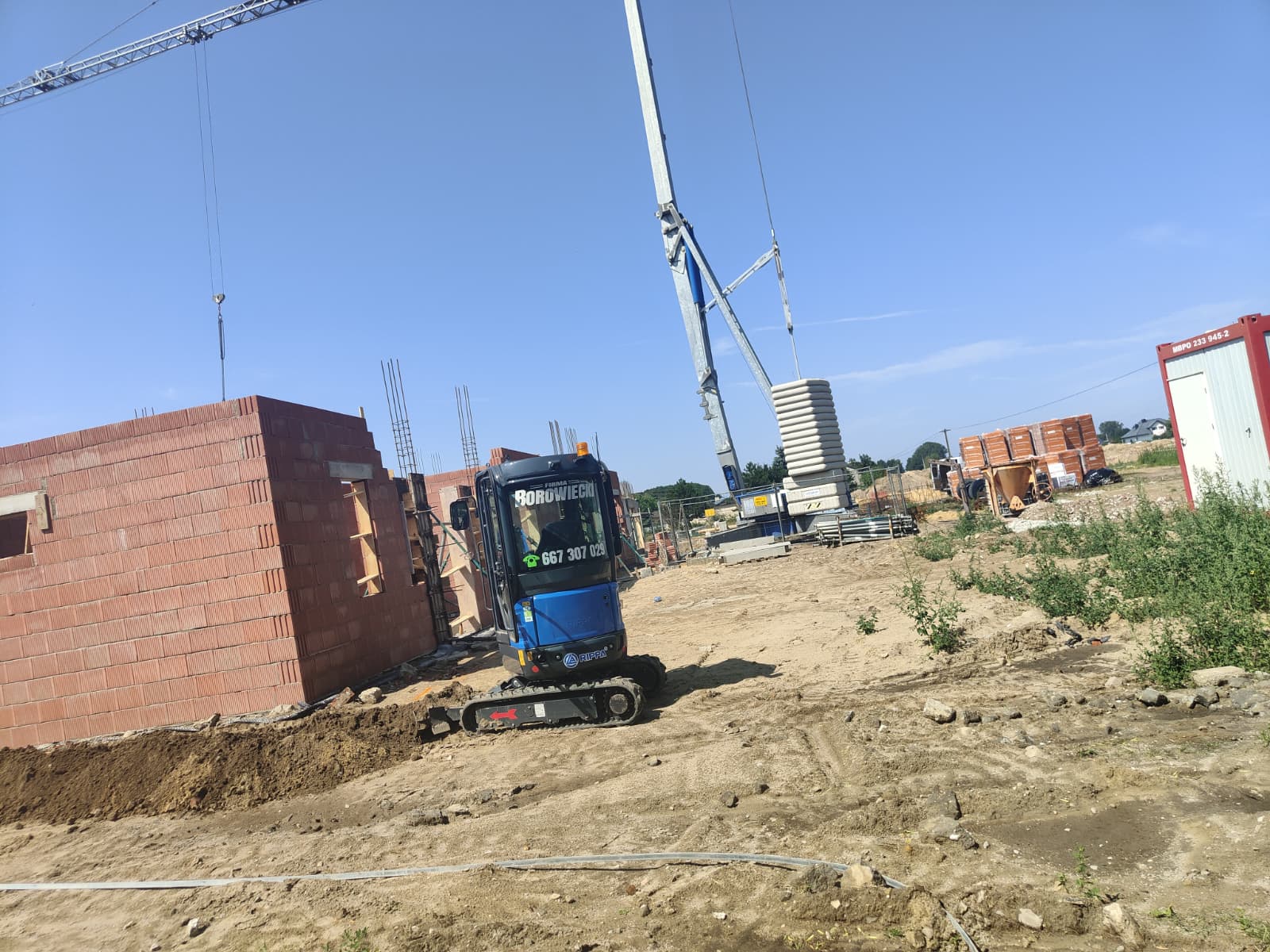 Minikoparka na budowie domu z dźwigiem w tle