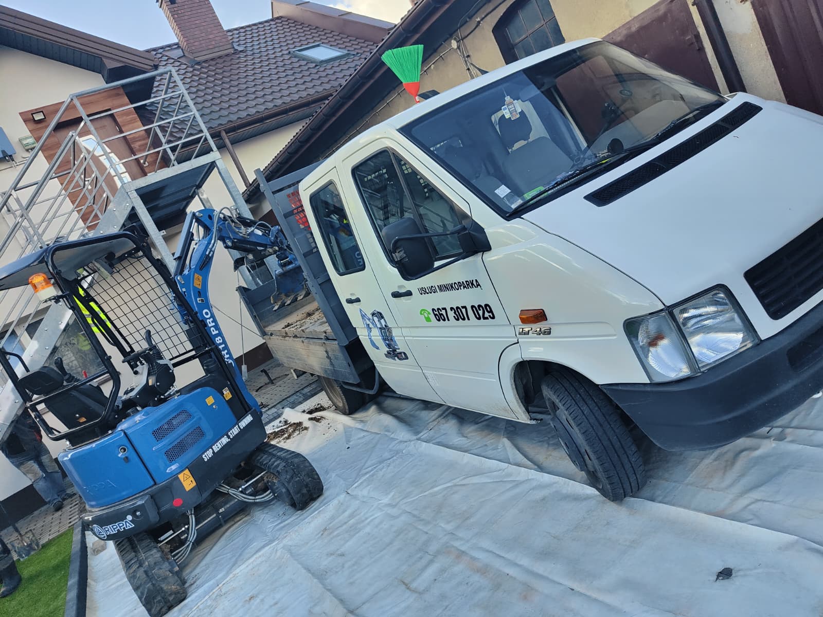 Minikoparka i auto firmowe na podjeździe zabezpieczonym folią